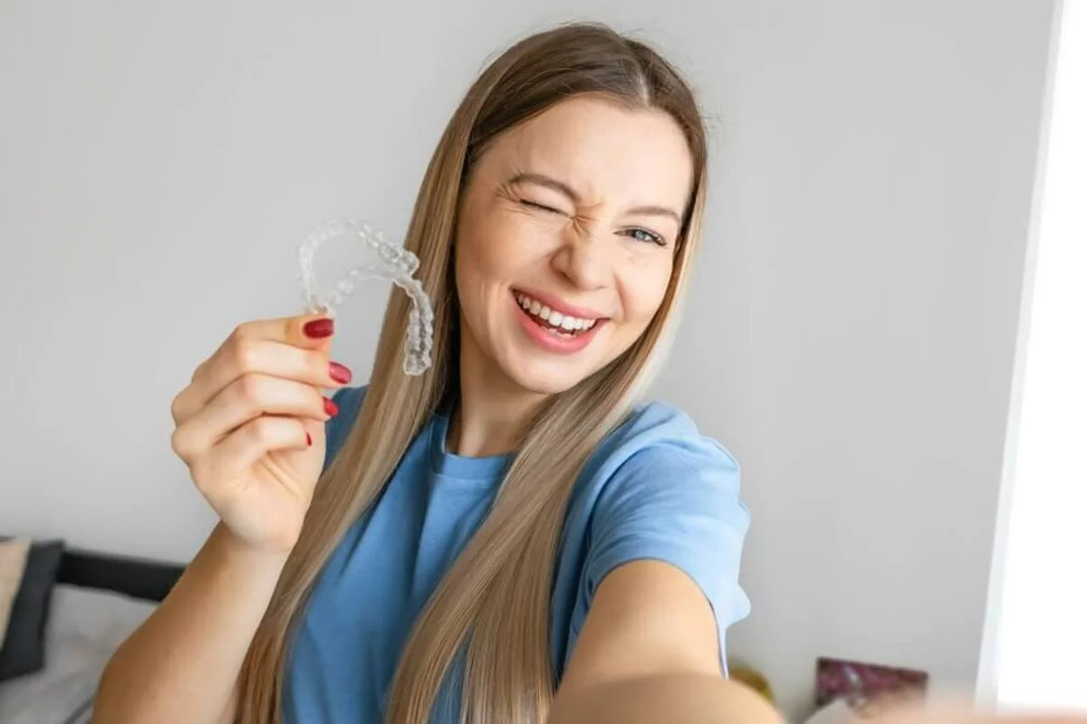 Woman smiling while holding a clear dental aligner