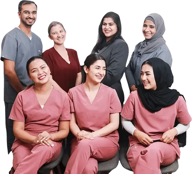Seven Pearl Dental Care team members smiling in a group portrait, three seated in pink scrubs